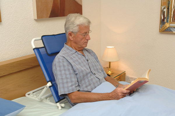 Individual using blue adjustable back support to sit up in bed and read. 