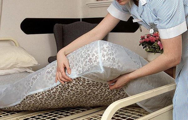 Healthcare worker demonstrating the translucent mattress cover being placed over a floral black and white mattress. 