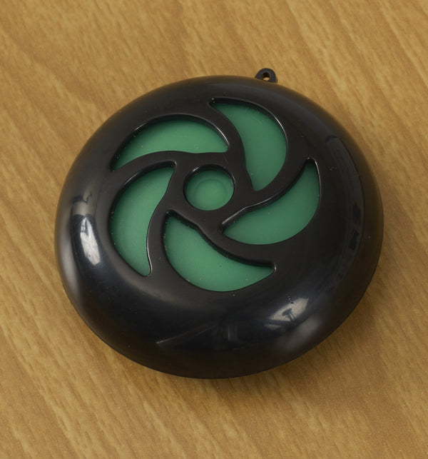 Circular black magiplug with green design around a circle in the middle. The product is shown against brown wooden background. 