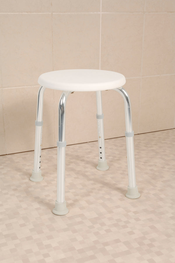 This image shows the shower stool, with a white round seat and four silver legs, in a cream bathroom. 