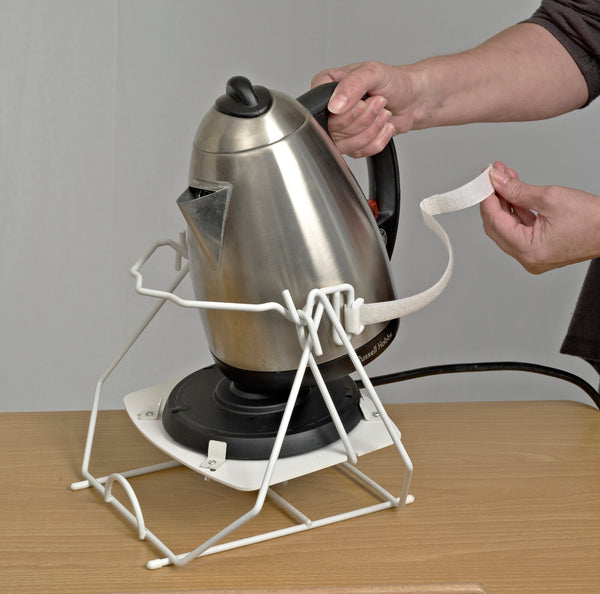 Image shows someone strapping a silver kettle into the white kettle tipper, on a wooden table. 