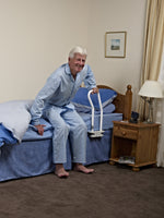 Individual in blue pajamas in a blue bed demonstrating use of the bed rail, shown to be attached under the mattress. 