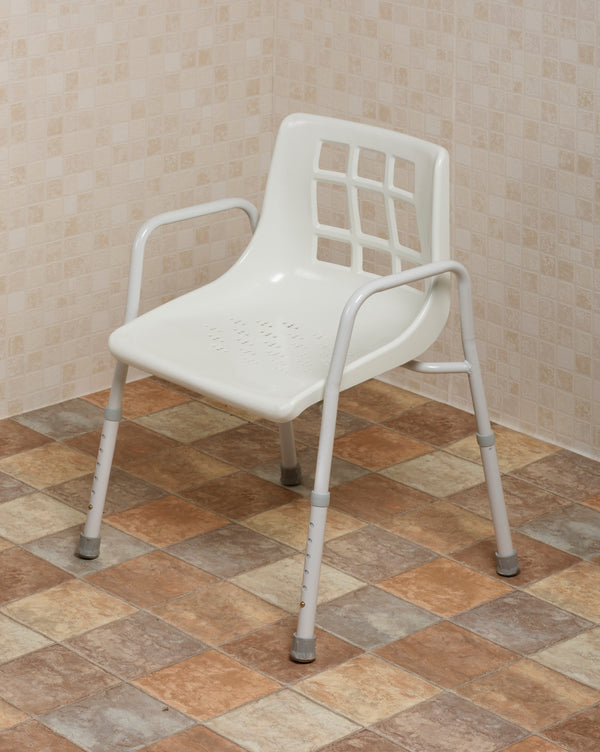 This image shows the white shower chair with adjustable legs, and grey grips on the feet, in a bathroom with cream tiled walls and beige tiled floor.