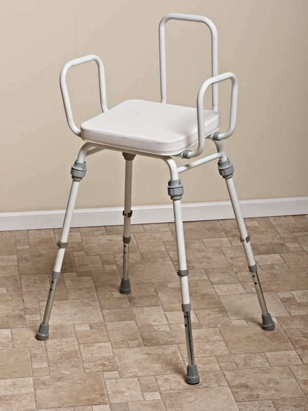 White four legged chair, with adjustable height and arm rests, against a cream wall and brown tiled floor. 