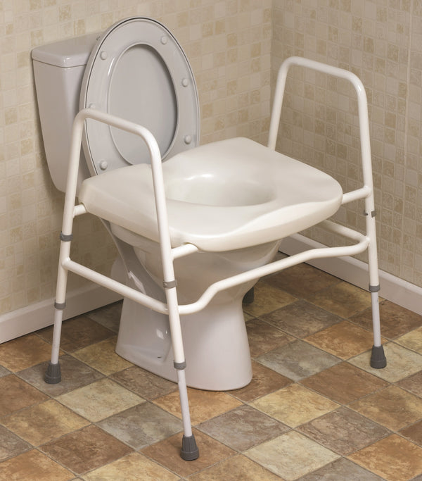 Image shows the white toilet frame and seat in place over a white toilet, in a bathroom with cream tiled walls, and beige tilled floors. 