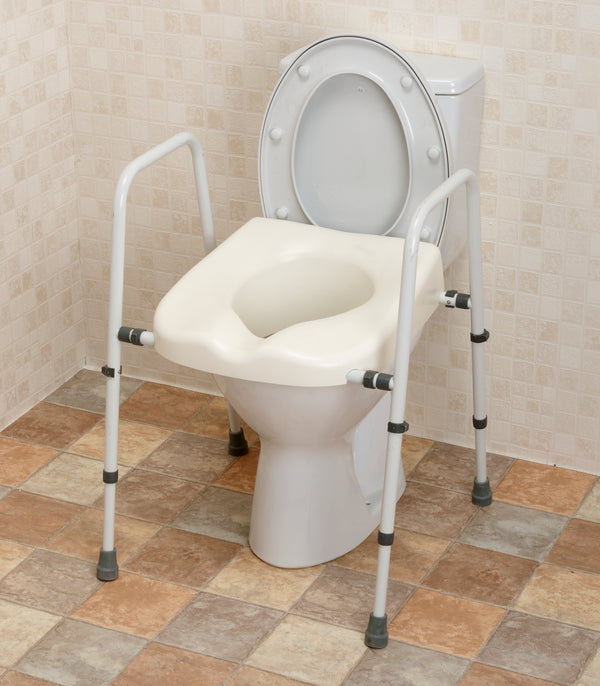 This image shows the white toilet frame and seat set up over a white toilet, in a bathroom with cream tiled walls and beige tilled floor. 