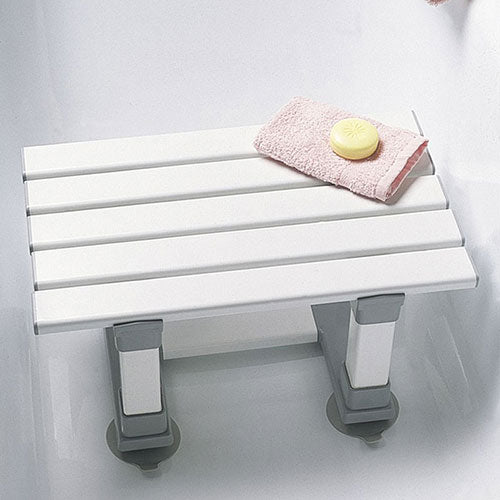 This image shows the slatted bath seat set up in a white shower with a pink flannel and yellow bar of soap resting on it. 