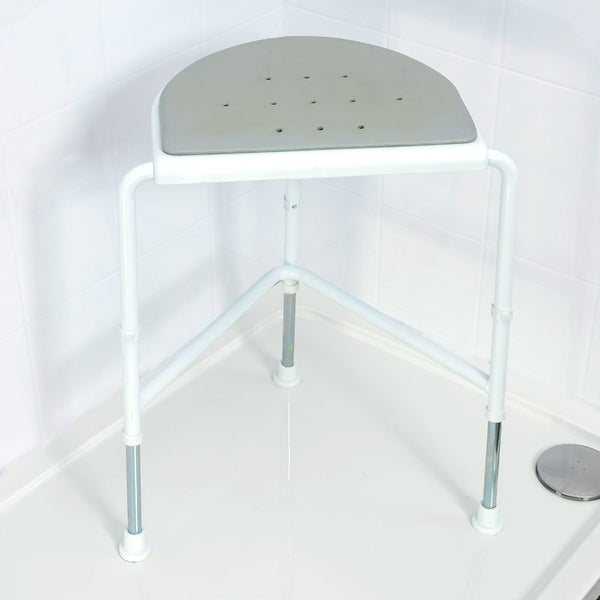 Image shows the product in place in the corner of a white tiled shower. The product has a three legged white frame and a curved edged grey cushion to fit into the corner of the shower.
