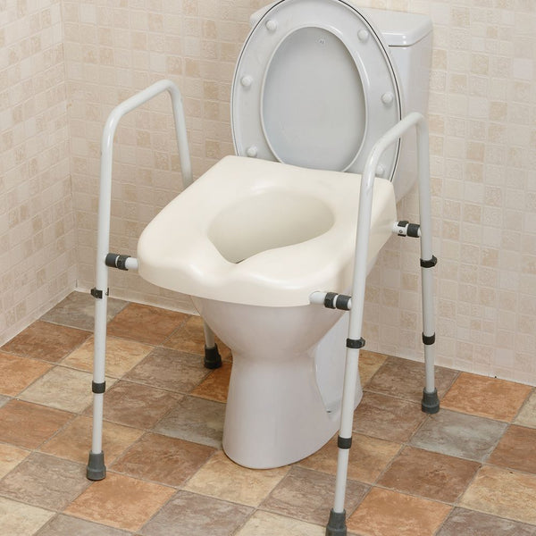 This image shows the white and grey toilet frame and toilet seat set up over a white toilet. This is in a bathroom with a cream tiled wall and brown tiled floor.