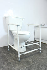 Image shows white frame with grey feet and adjustable width points, around a white toilet, in a white bathroom with grey floor. 