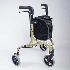 Image shows three wheeled champagne and black rollator with black storage bag between the handles. The small grey and black wheels, and black handles and break system are also clear, against the white background. 