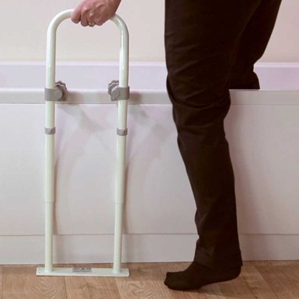 Image shows someone using the white version of the bath rail to step safely into a bath. 