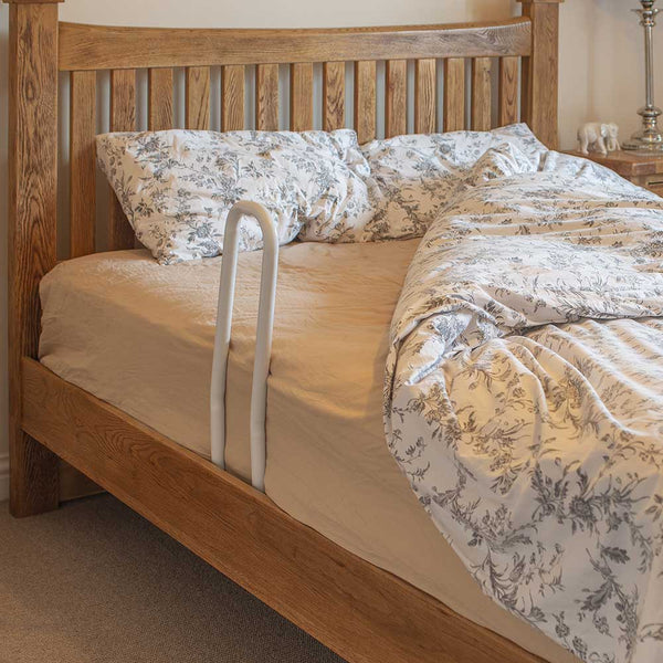 Demonstrates white rail set up at the edge of a wooden double bed with floral white and grey bedding. 